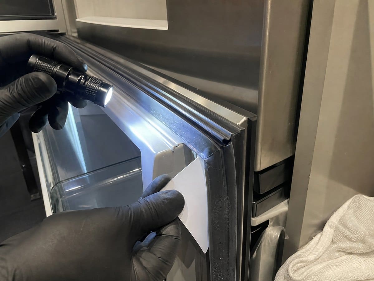 Close-up of a refrigerator door gasket being inspected for condensation and seal gaps