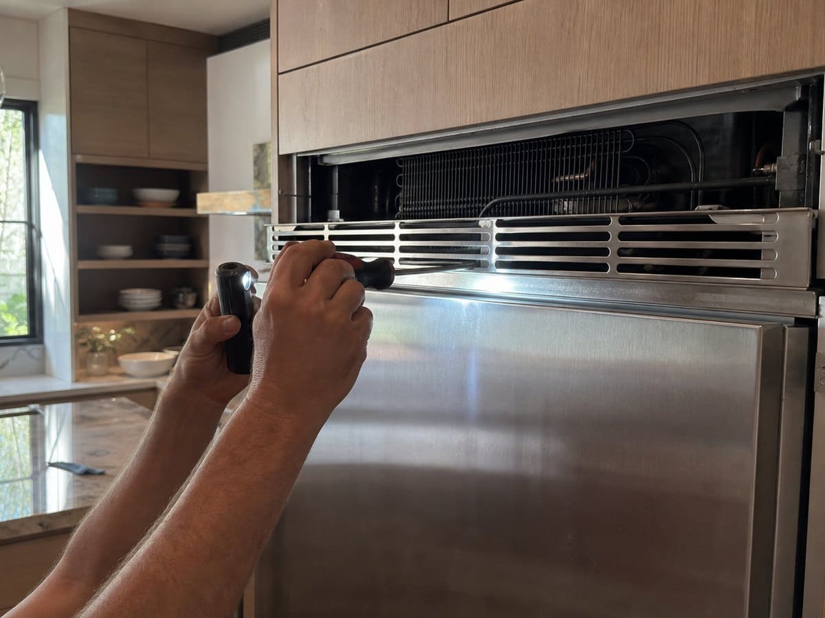 Technician working on a built-in refrigerator service panel in a custom Montclair kitchen