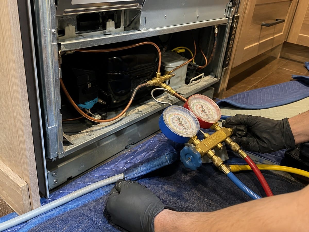 Technician working near a compressor and sealed-system access area on a built-in refrigerator